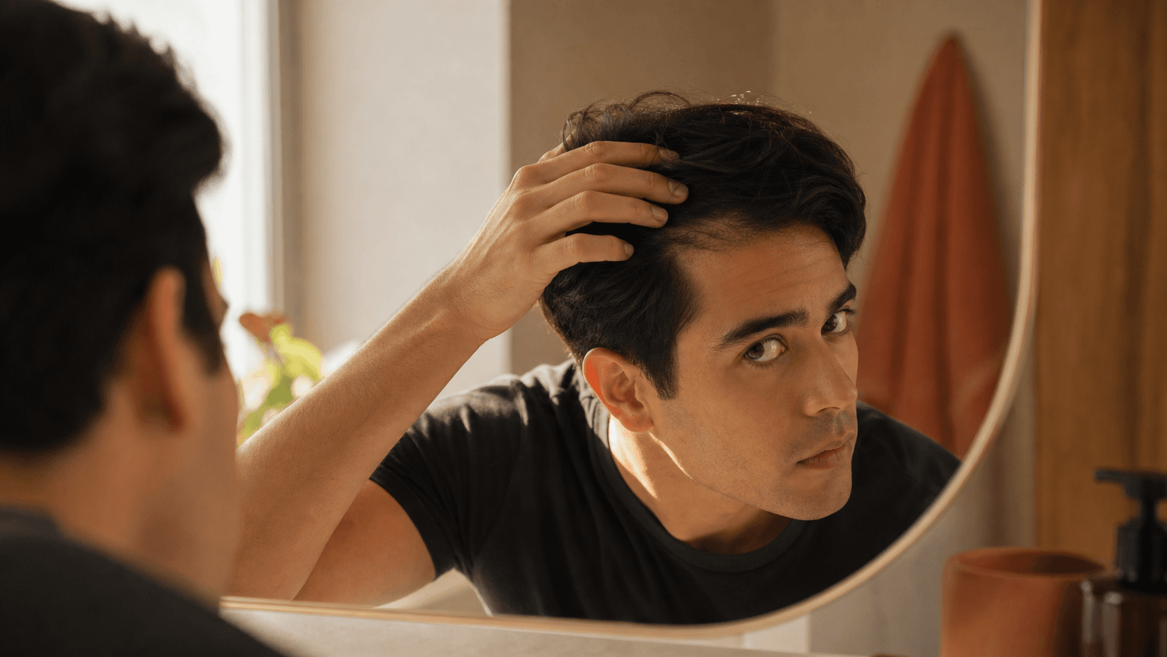 Young adult checking a receding hairline at 25 in a warm bathroom mirror with natural light