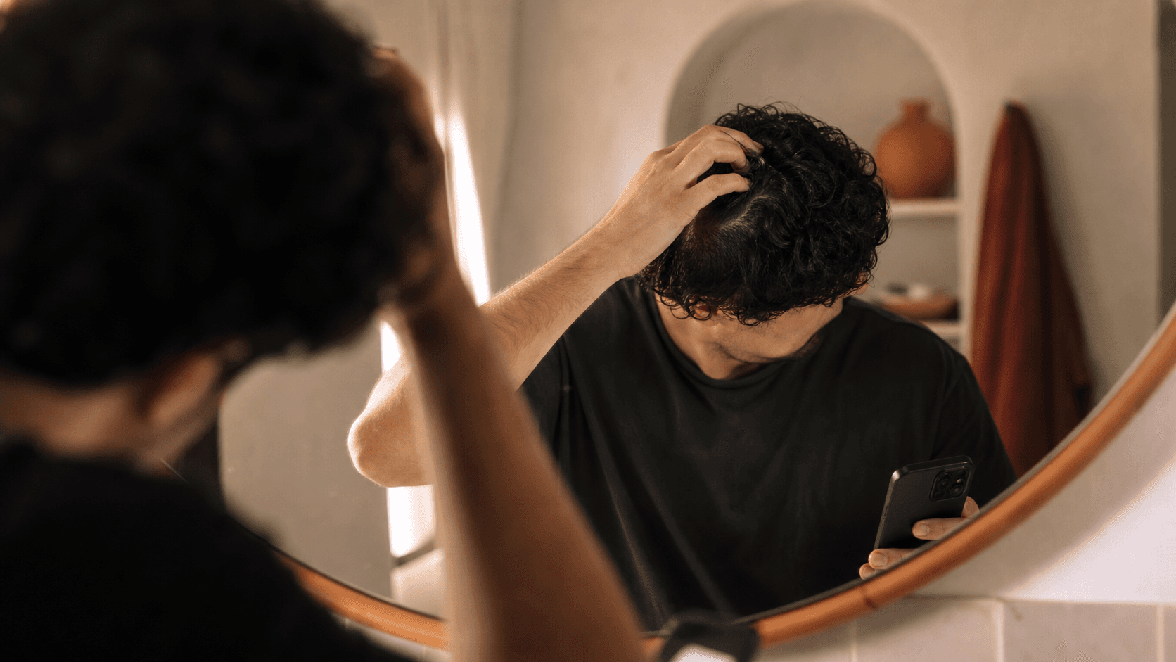 Person checking early hair loss signs around the crown in a warm bathroom mirror scene